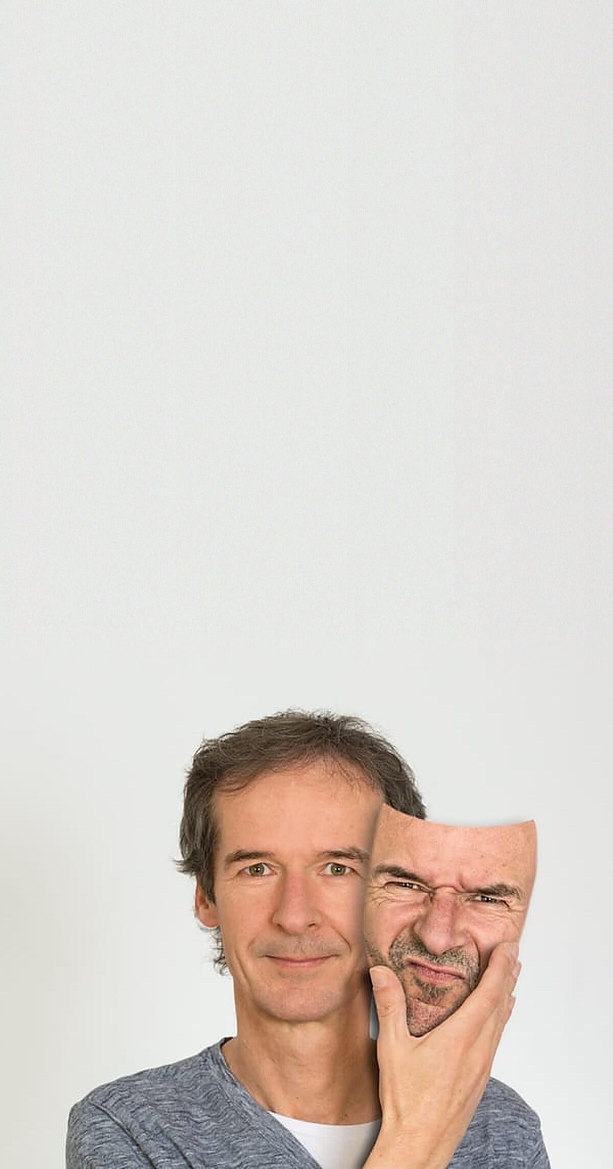 Peter Seitz vor heller Wand, ruhig lächelnd, hält eine verzerrte Gesichtsmaske neben sein Gesicht